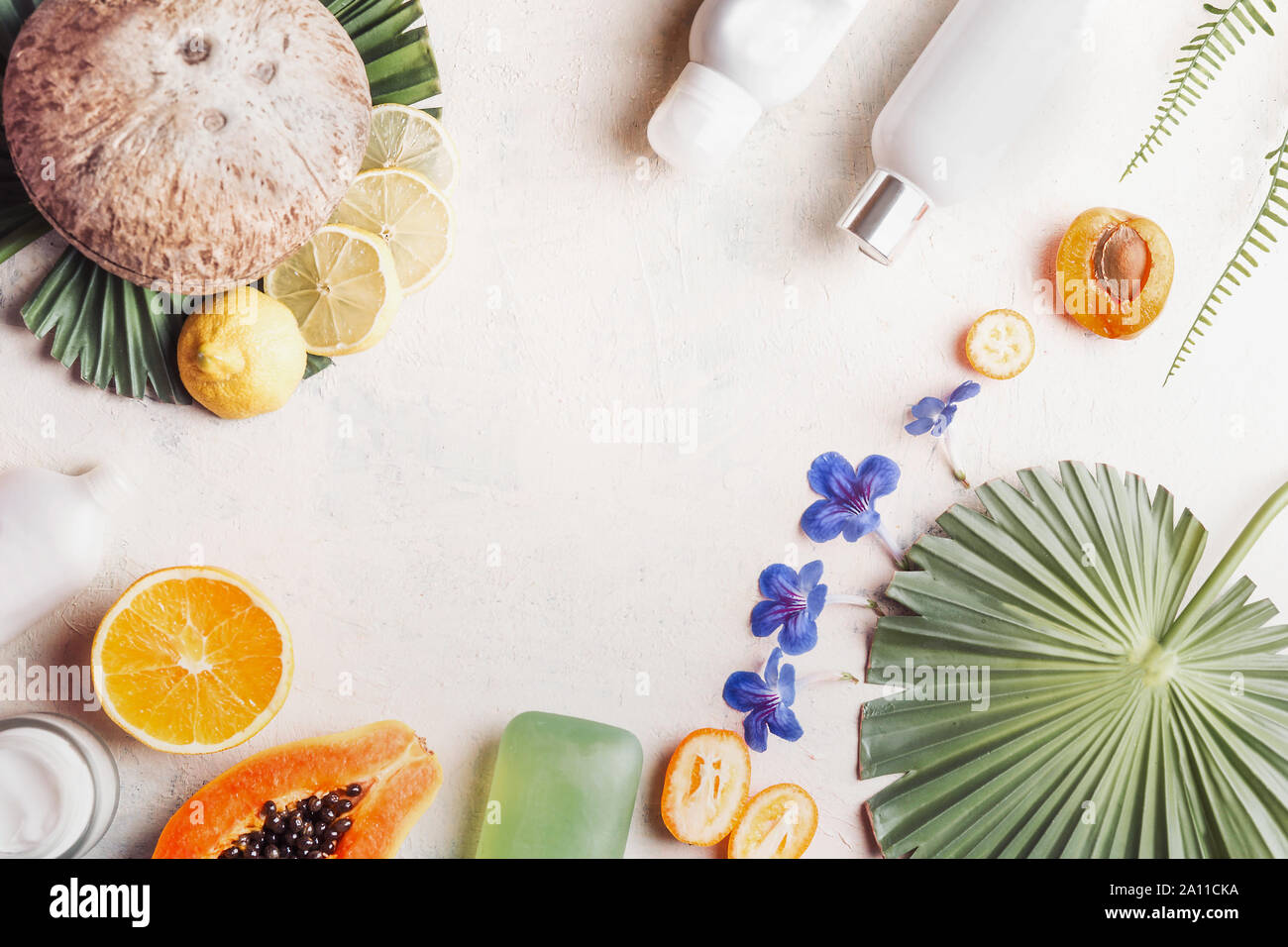 Umweltfreundliche vegane Kosmetika auf weißem Schreibtisch mit Kokosnuss, Früchte, Blumen und tropischen Blättern, Ansicht von oben. Gesunde Lebensweise. Natura Stockfoto