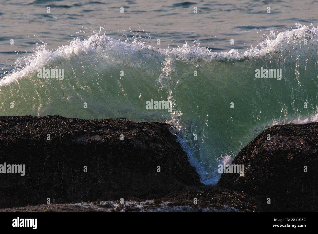 Eine Welle Überspannungen in das Meer zu einem Felsvorsprung, als es über der Oberfläche explodiert Stockfoto