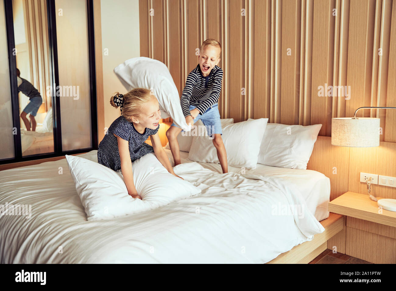 Adroable kleiner Bruder und Schwester lachend, während eine Kissenschlacht zusammen auf ihrem Bett zu Hause Stockfoto