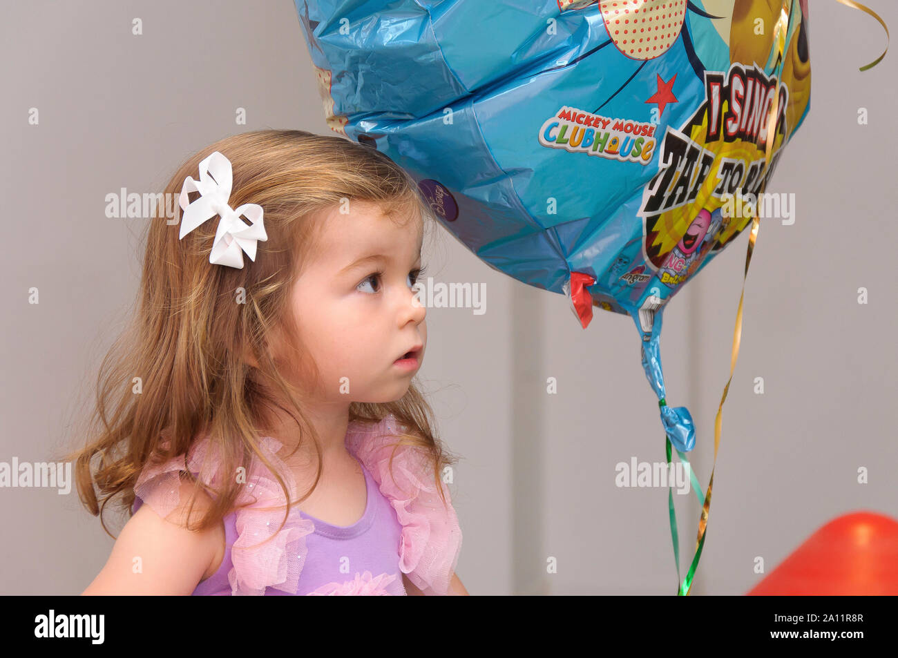 Ein ehrliches, authentisches Porträt eines niedlichen, zwei Jahre alten blonden Mädchens mit einem Ballon auf einer Kinderparty Stockfoto