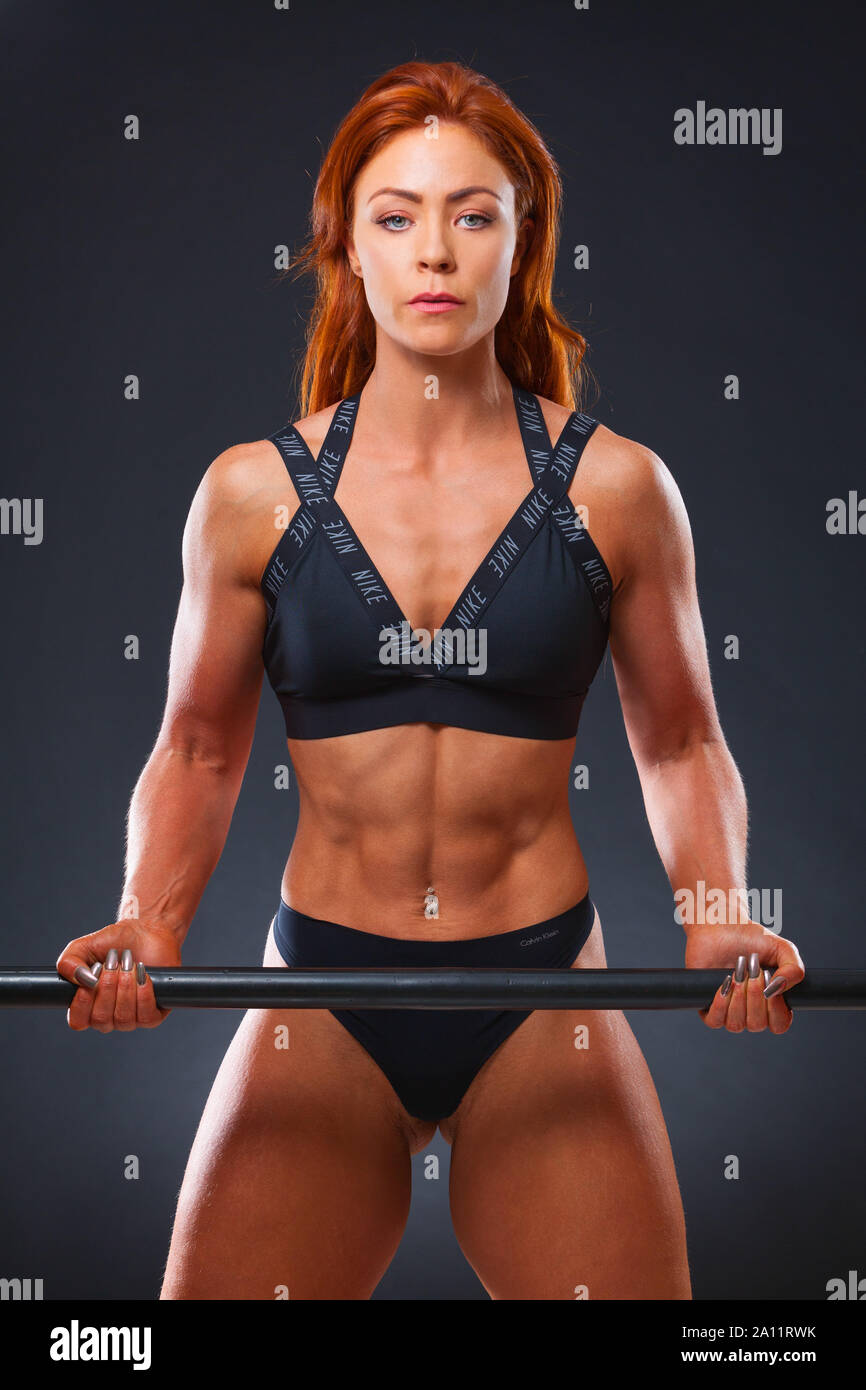 Eine junge rothaarige Frauen Fitness Modell ihre Muskeln in einem Studio Einstellung mit schwarzem Hintergrund Stockfoto