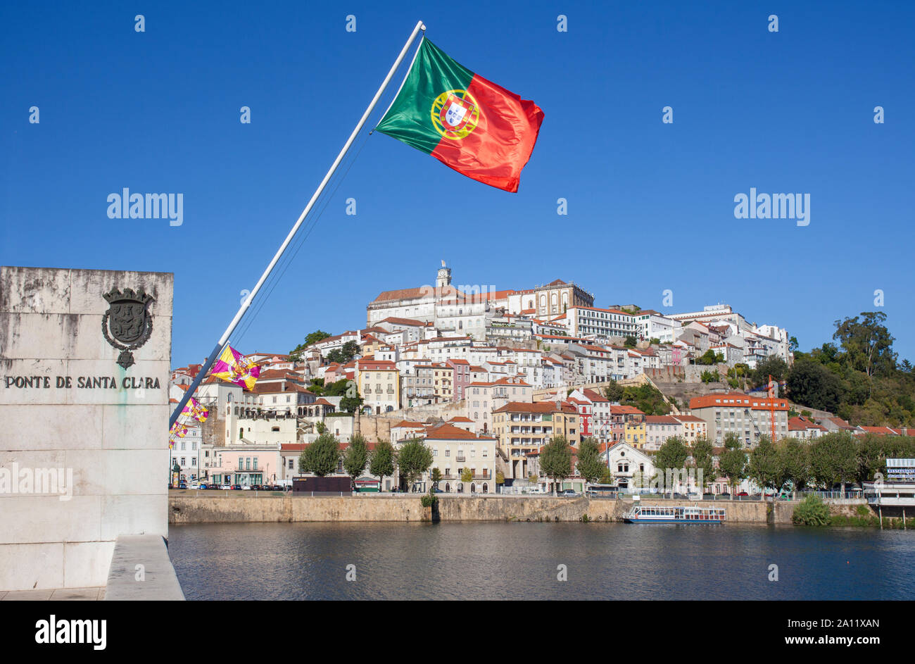 Blick auf die Altstadt von Coimbra aus Santa Clara Brücke mit Portugal Flagge das Weben in den blauen Himmel. Coimbra ist eine wunderschöne historische Stadt mit vielen touristischen sp Stockfoto