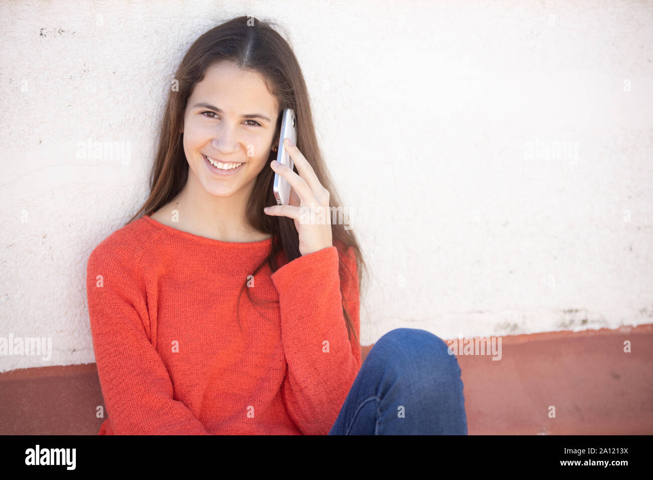 Chica adolescente Feliz por teléfono Móvil sentada hablando en La Azotea Stockfoto