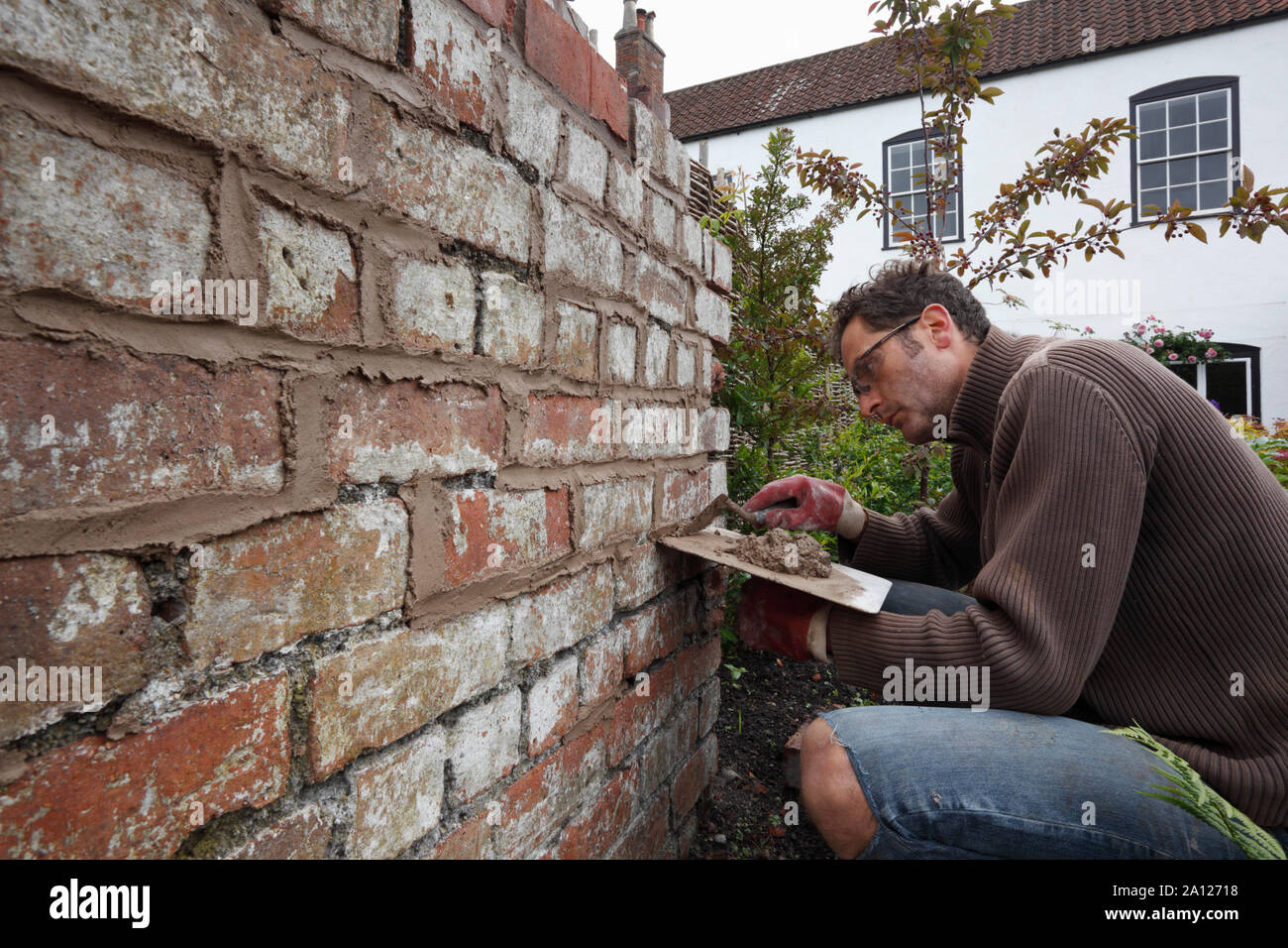 Repointing einer alten Mauer mit Kalkmörtel. 3 Bild-Serie. Bild Nummer 1 von 3. Stufe 1, Mörtel drücken in die Lücken ein. Stockfoto