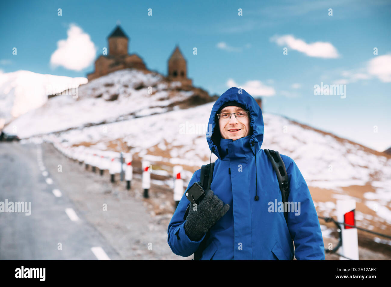 Stepantsminda, Gergeti, Georgia. Man Touristen Backpacker reisenden Fotografen posiert in der Nähe der Kirche der Heiligen Dreifaltigkeit - Tsminda Sameba. Schönen georgianischen Lan Stockfoto