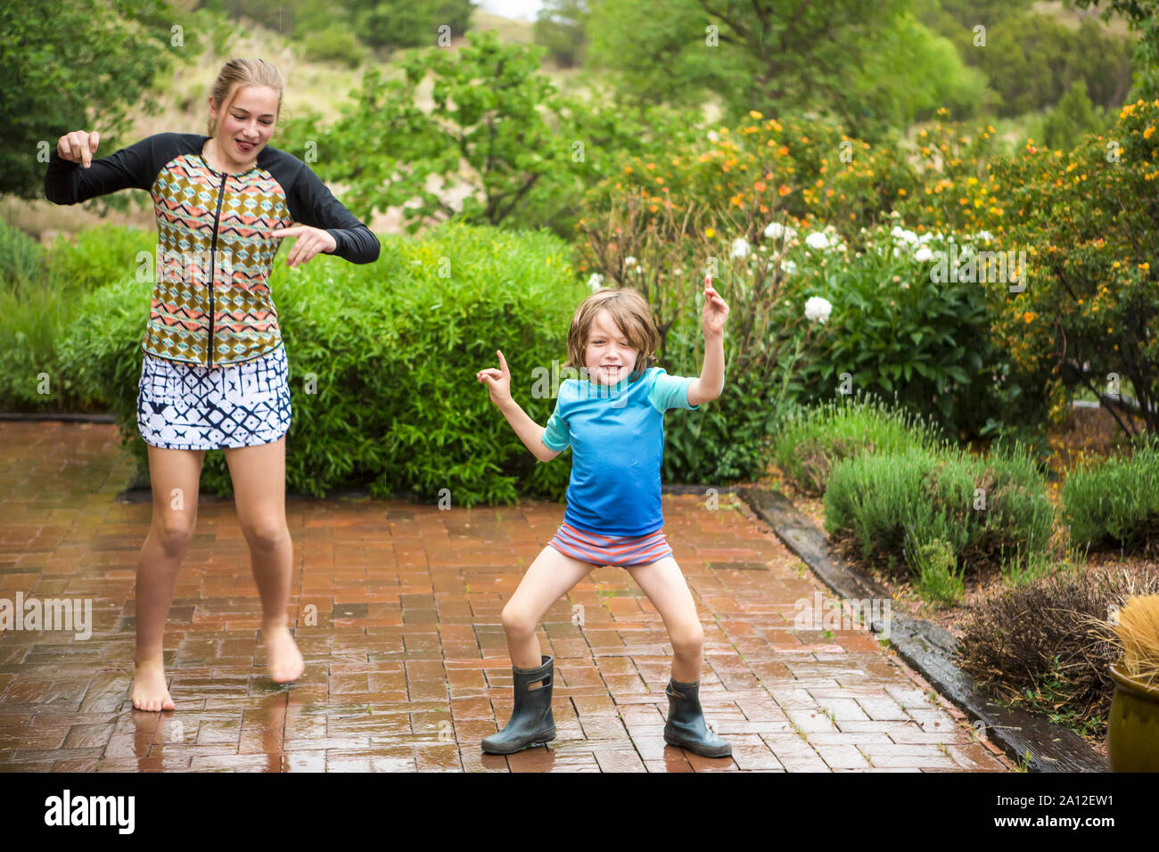 5 Jahre alten Jungen und seine 13 Jahre alte Schwester tanzen im Regen. Stockfoto