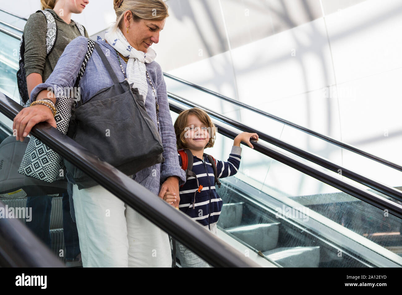 Lächelnd 5 Jahre alten Jungen auf Flughafen Rolltreppe mit seiner Mutter und der älteren Schwester Stockfoto