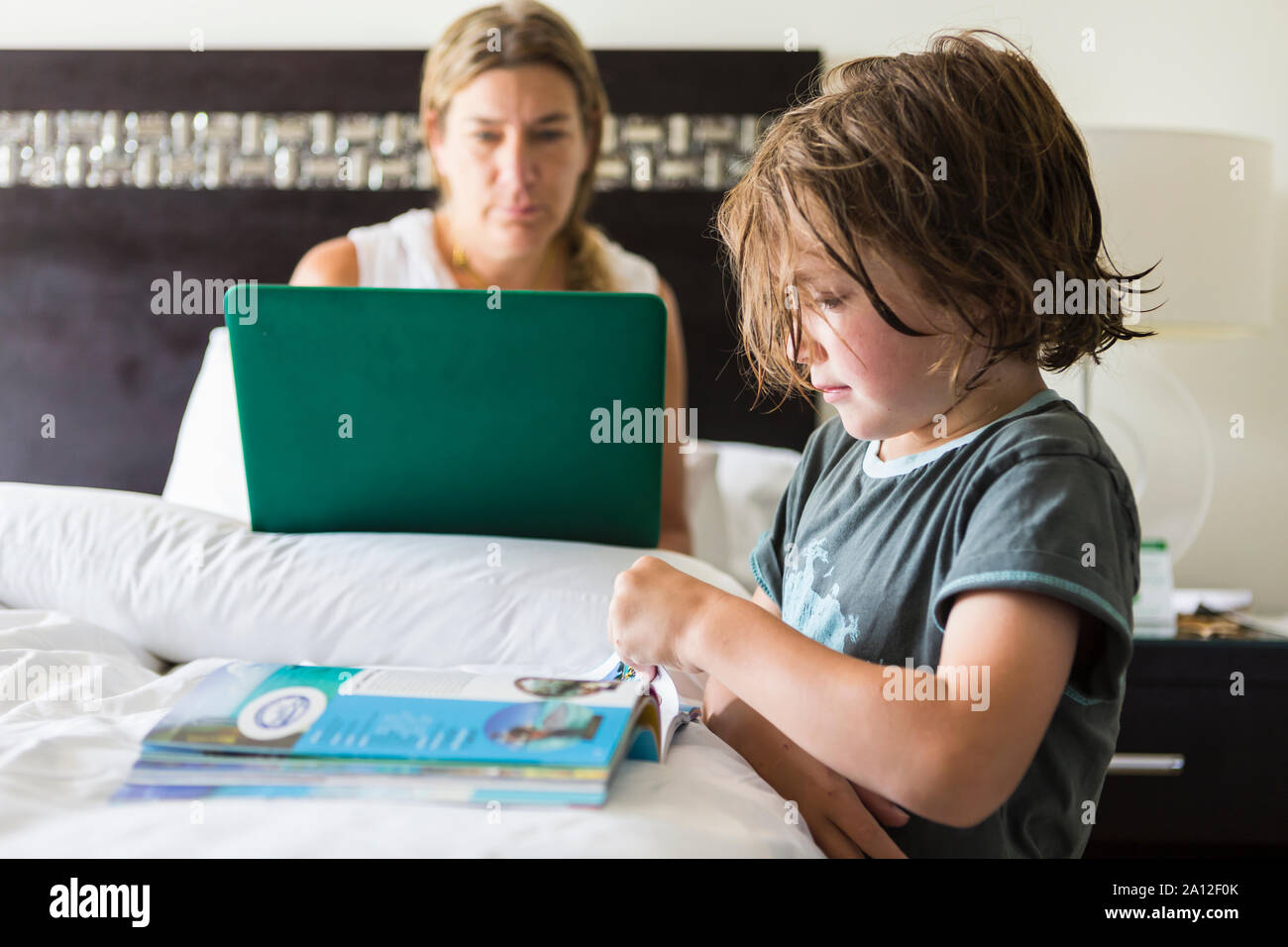 5 Jahre alter Junge, buchen Sie im Hotel Zimmer als Mom funktioniert auf dem Laptop Stockfoto