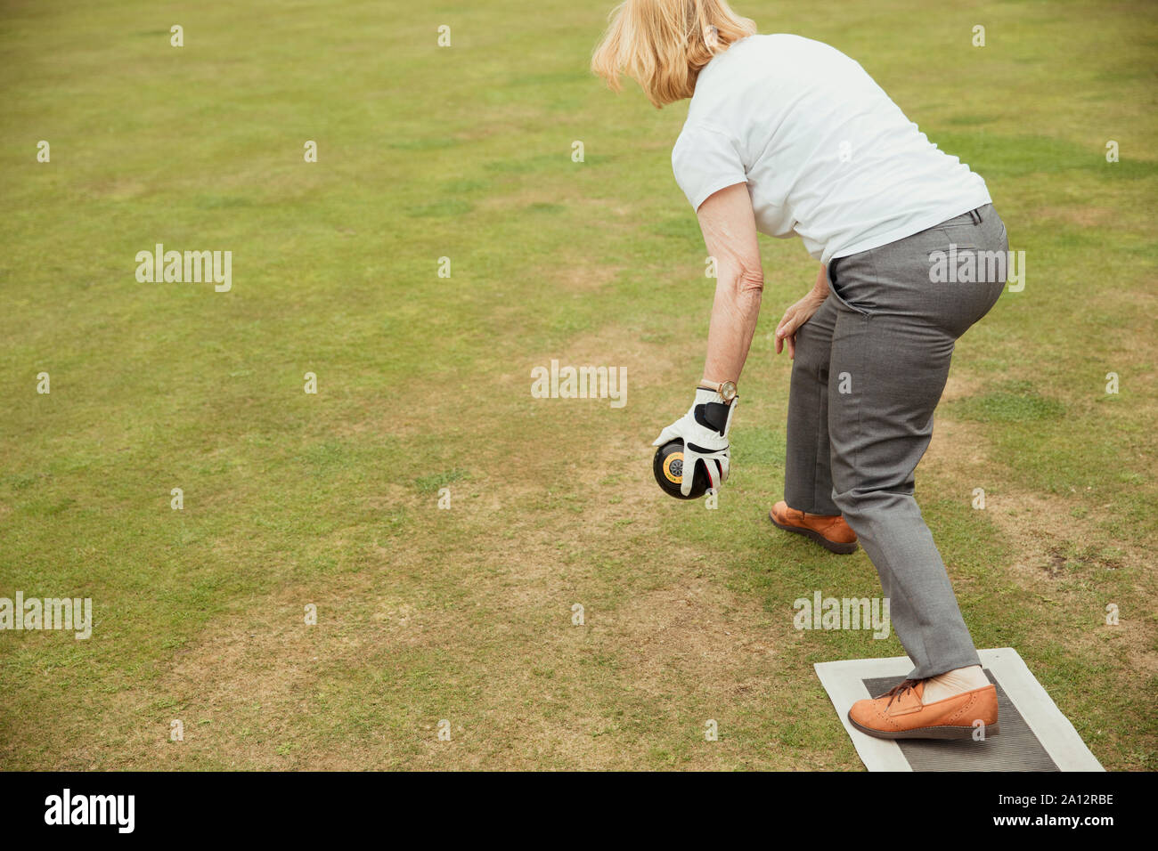Eine Ansicht von hinten geschossen von einer älteren Frau mit einem Boccia, bereit, ihr Schuß in einem Lawn Bowling Spiel zu nehmen. Stockfoto