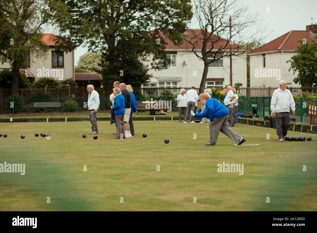 Eine Seitenansicht geschossen von einer älteren Frau, die ihre Aufnahme in ein Spiel der Lawn Bowling, die von anderen Senioren in der Gemeinschaft umgeben. Stockfoto