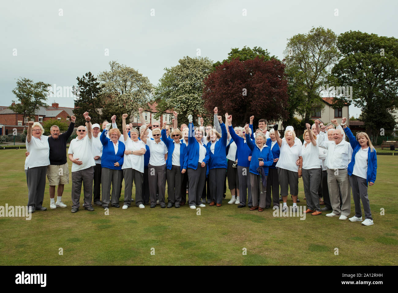 Einen weiten Blick geschossen von einer Gemeinschaft von Senioren Stanzen der Luft, feiert, nachdem ihre Lawn Bowling Spiel. Stockfoto