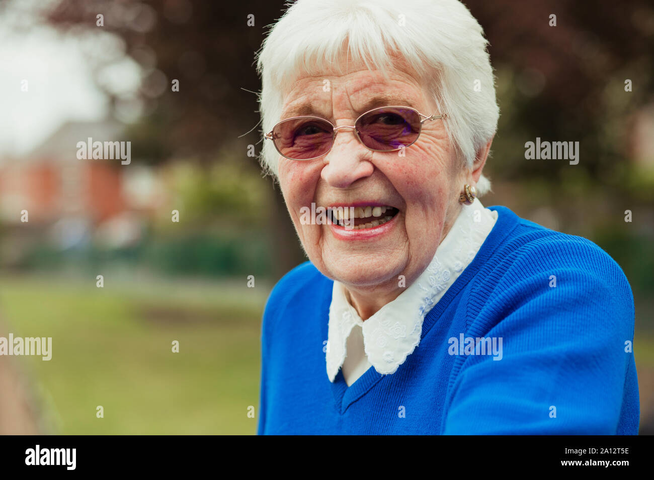 Eine Nahaufnahme von einer älteren Frau lächelnd in die Kamera schaut. Sie trägt rosa Sonnenbrille. Stockfoto