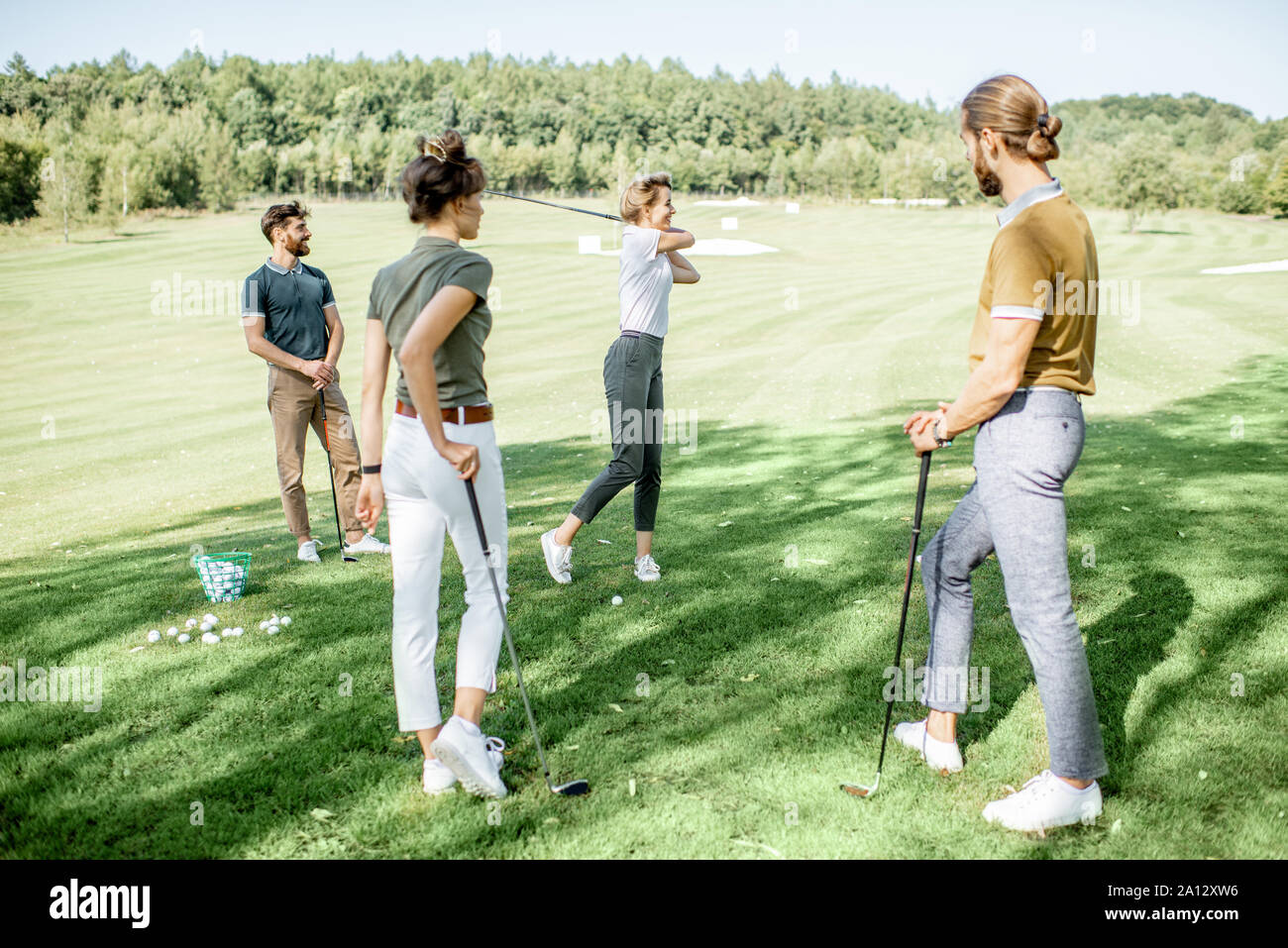Gruppe von einem jungen Menschen lässig gekleidet, Golf spielen auf dem Golfplatz an einem sonnigen Tag, Frau Schwingen einen Putter Stockfoto
