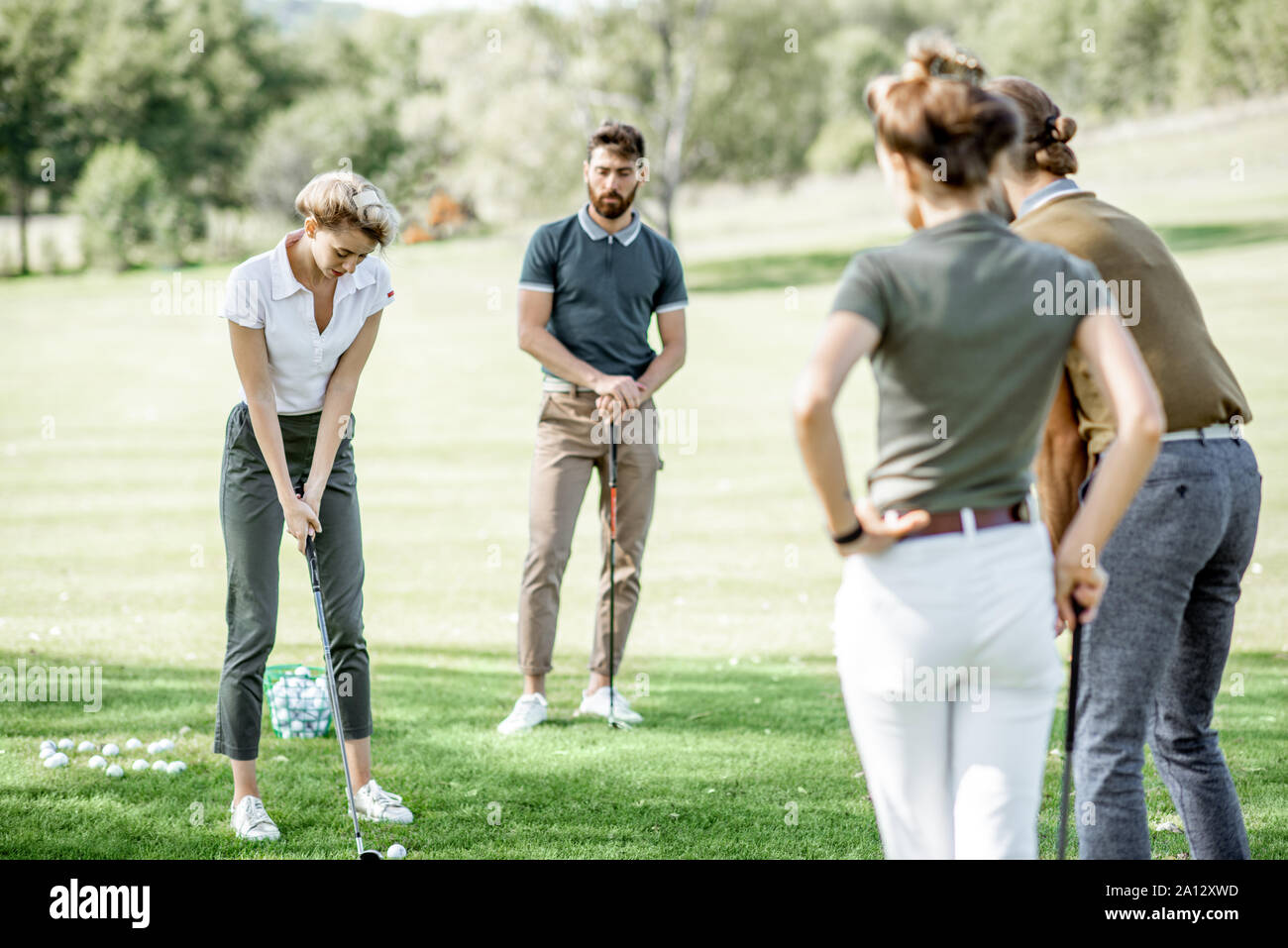 Gruppe von einem jungen Menschen lässig gekleidet, Golf spielen auf dem Golfplatz an einem sonnigen Tag, Frau Schwingen einen Putter Stockfoto