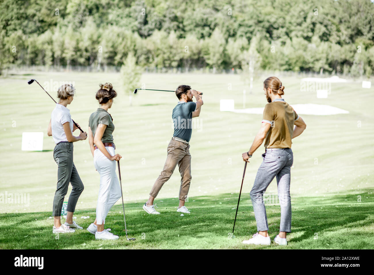 Gruppe von einem jungen Menschen lässig gekleidet, Golf spielen auf dem Golfplatz an einem sonnigen Tag, man Schwingen einen Putter Stockfoto