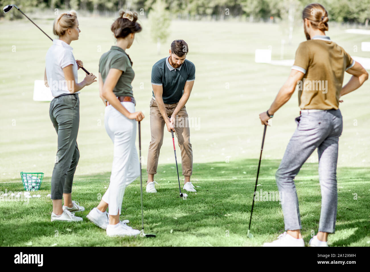 Gruppe von einem jungen Menschen lässig gekleidet, Golf spielen auf dem Golfplatz an einem sonnigen Tag, man Schwingen einen Putter Stockfoto