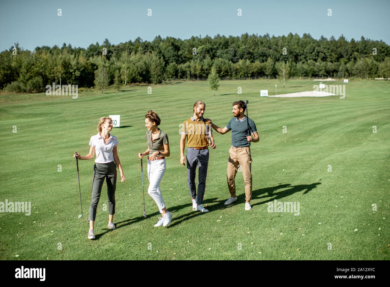 Gruppe von Freunden reden und gehen mit Putter beim Golf spielen auf den schönen Kurs an einem sonnigen Tag Stockfoto