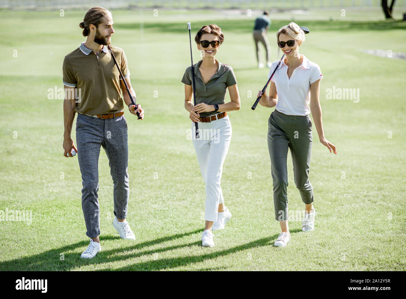 Junge Freunde lässig gekleidet gehen mit Putter auf dem Golfkurs während eines Spiels an einem sonnigen Tag Stockfoto