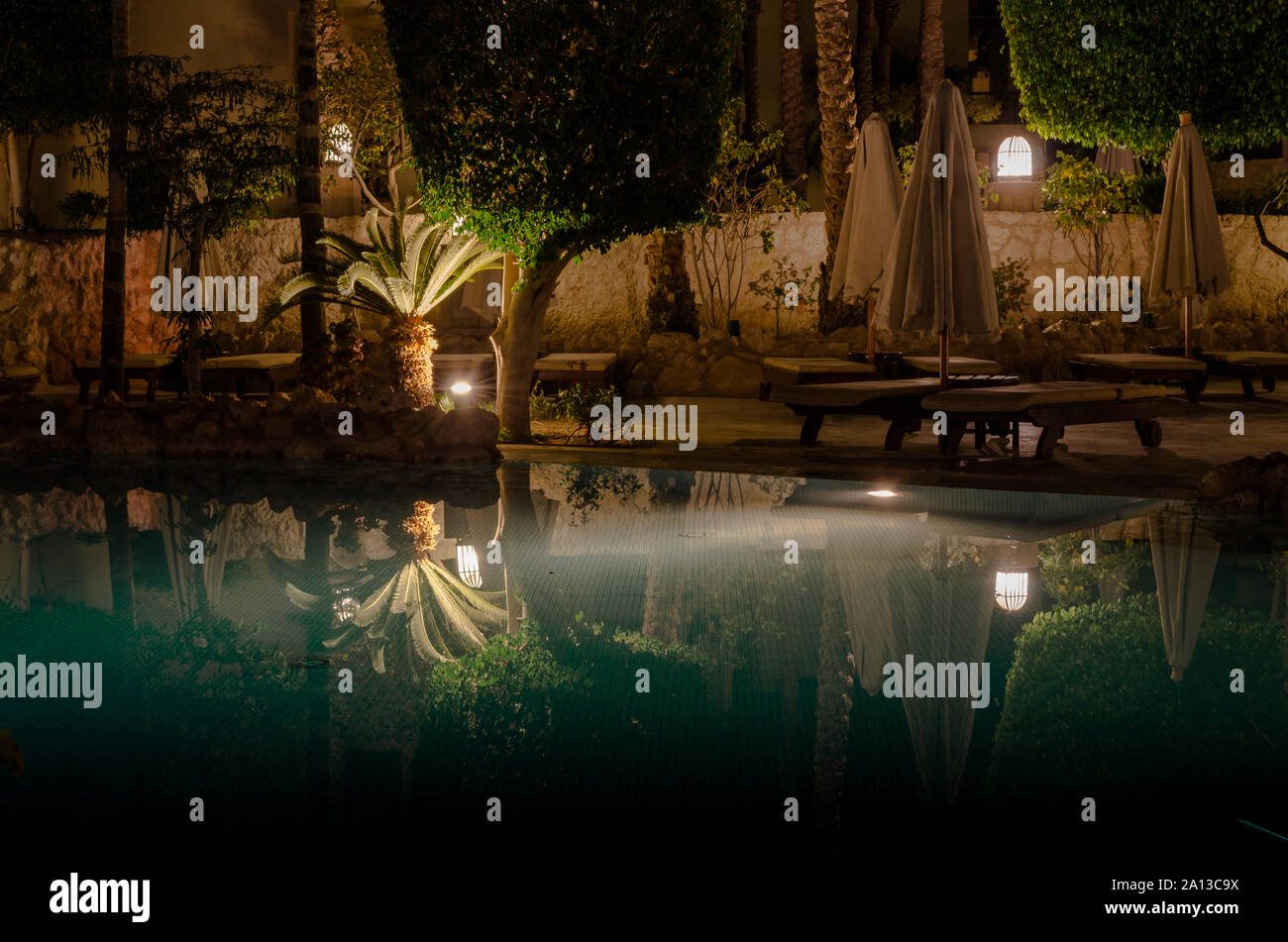 Sharm El Sheikh, Ägypten - 02 06 2018: Nacht im Hotel Aquamarine Pool gefaltet Sonnenschirme leer Holzliegen Palmen und dekorative Bäume lant Stockfoto