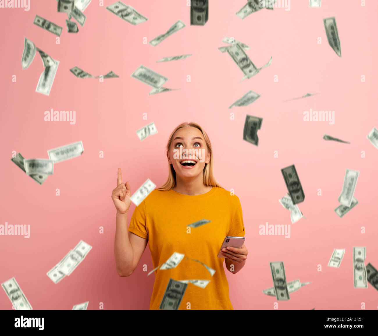 Blonde süße Mädchen gewinnt Geld mit Smartphone App. Erstaunt und überrascht Ausdruck Gesicht. Rosa Hintergrund Stockfoto