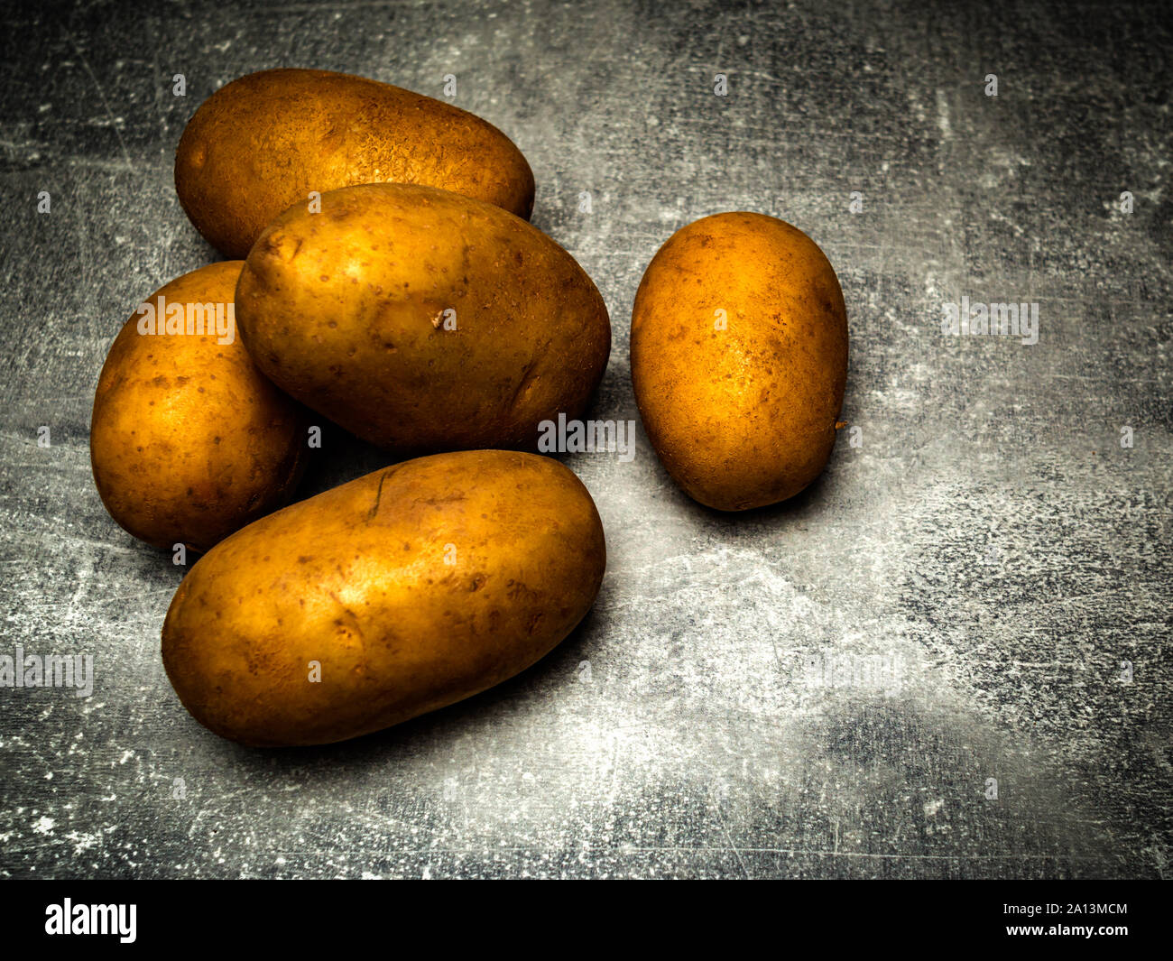 Fünf golden glänzend, roh chiaroscuro Kartoffeln auf grauem Hintergrund. Stockfoto