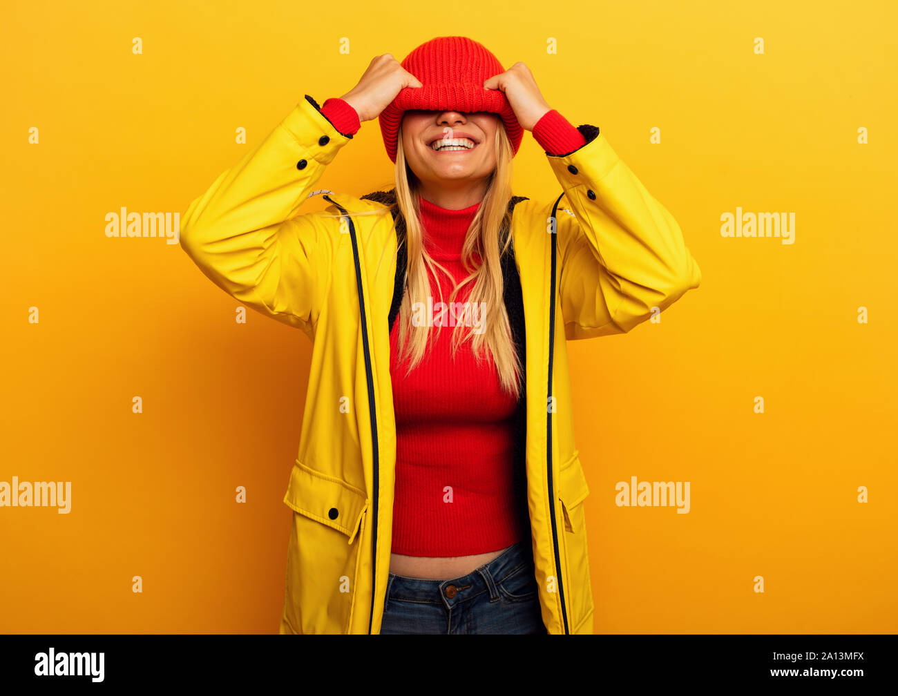 Mädchen mit Jacke auf gelben Hintergrund deckt ihr Gesicht mit ihren Hut für das Wetter Stockfoto