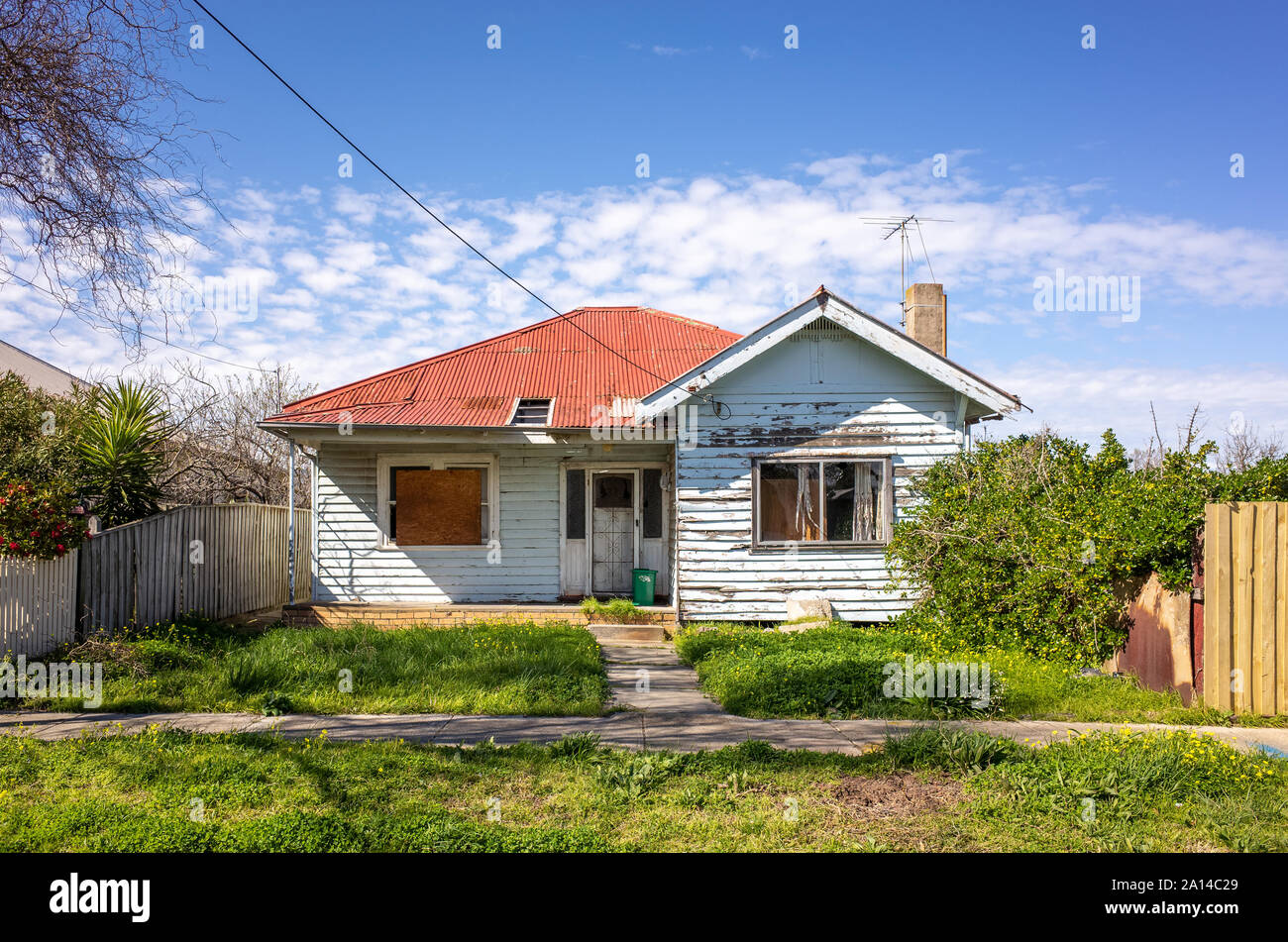 Ein altes und heruntergekommenes Wohnhaus mit einer unbeaufsichtigten Vorgarten. Australische weatherboard Home mit einem Wellblechdach. Stockfoto