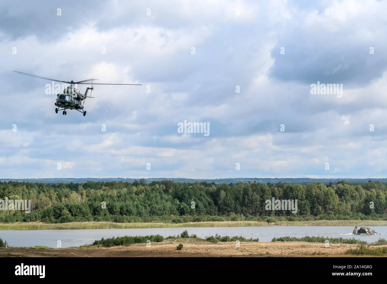 Ein Mi-8 Helikopter bietet Antenne Sicherheit, während eine PTS-2 Transporte Fahrzeuge und Personal über einen nassen Spalt während einer Demonstration für Verehrte Besucher als Teil der Schnellen Trident2019 in Combat Training Center-Yavoriv, Sept. 20, 2019. Stockfoto