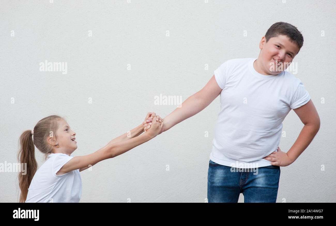 Schöne dünne Mädchen ziehen mit beiden Händen Fett starke Junge im weißen Hemd und Jeans hand auf hellen Hintergrund mit Kopie Raum Stockfoto