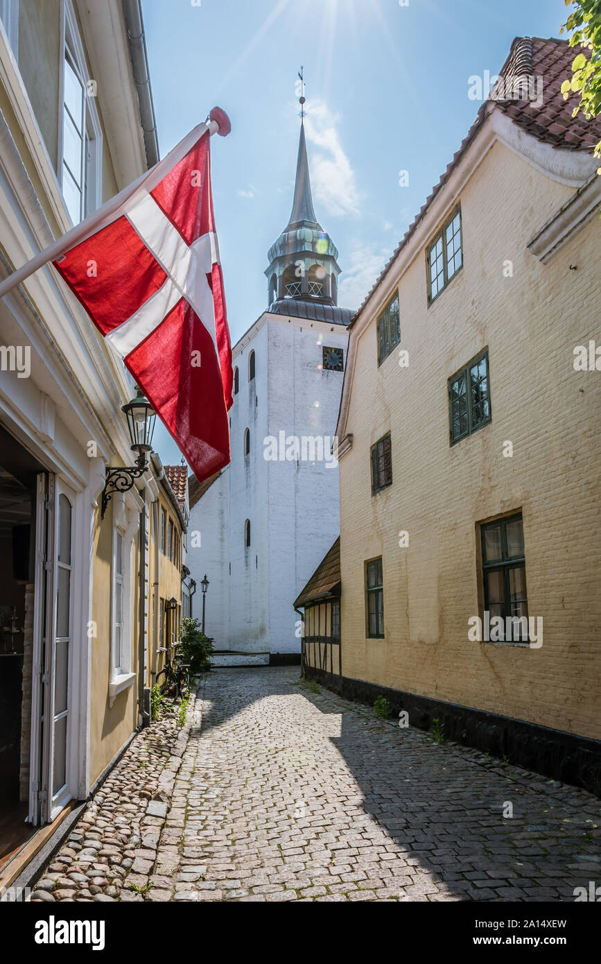 Die dänische Flagge hängen in eine enge Gasse mit der Kirche im Hintergrund, Aeroskobing, Dänemark, 13. Juli 2019 Stockfoto