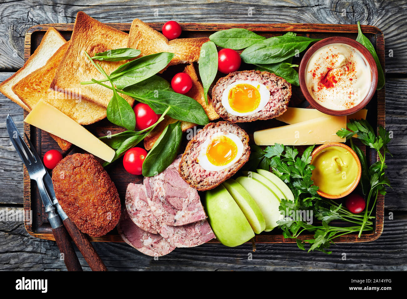 Pflüger's Mittagessen von Toast, Cheddar Käse Keile, Apple, schottische Eier, geschnitten headcheese, Tomaten, Spinat, hot Senf serviert auf einem Holz- Fach auf eine Stockfoto