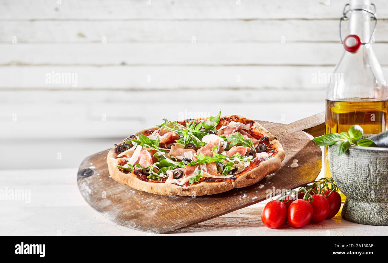 Spezialität Backofen befeuert Prosciutto italienische Pizza mit frischem Rucola Parmesan auf eine knusprige Kruste auf einem alten Paddel aus Holz mit frischen Zutaten, cop Stockfoto