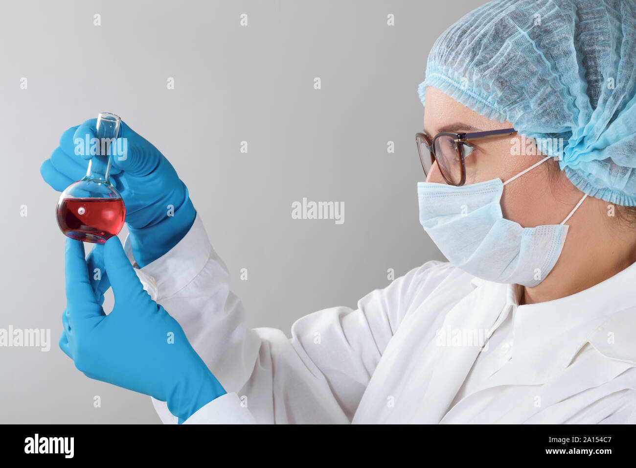In einem Chemielabor, ein weiblicher Apotheker ist die Analyse eine Flasche mit roter Flüssigkeit. Medizinischen Experiment mit einem Rohr. Chemiker arbeitet auf einem Test mit blauen glov Stockfoto
