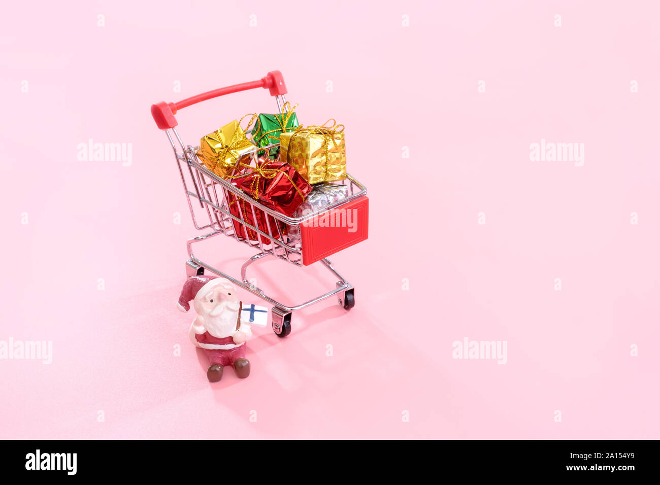 Christmas shopping Konzept, mini Rot Warenkorb Trolley mit Santa Claus Spielzeug und Geschenkbox auf rosa Hintergrund, leere Kopie Platz, in der Nähe Stockfoto