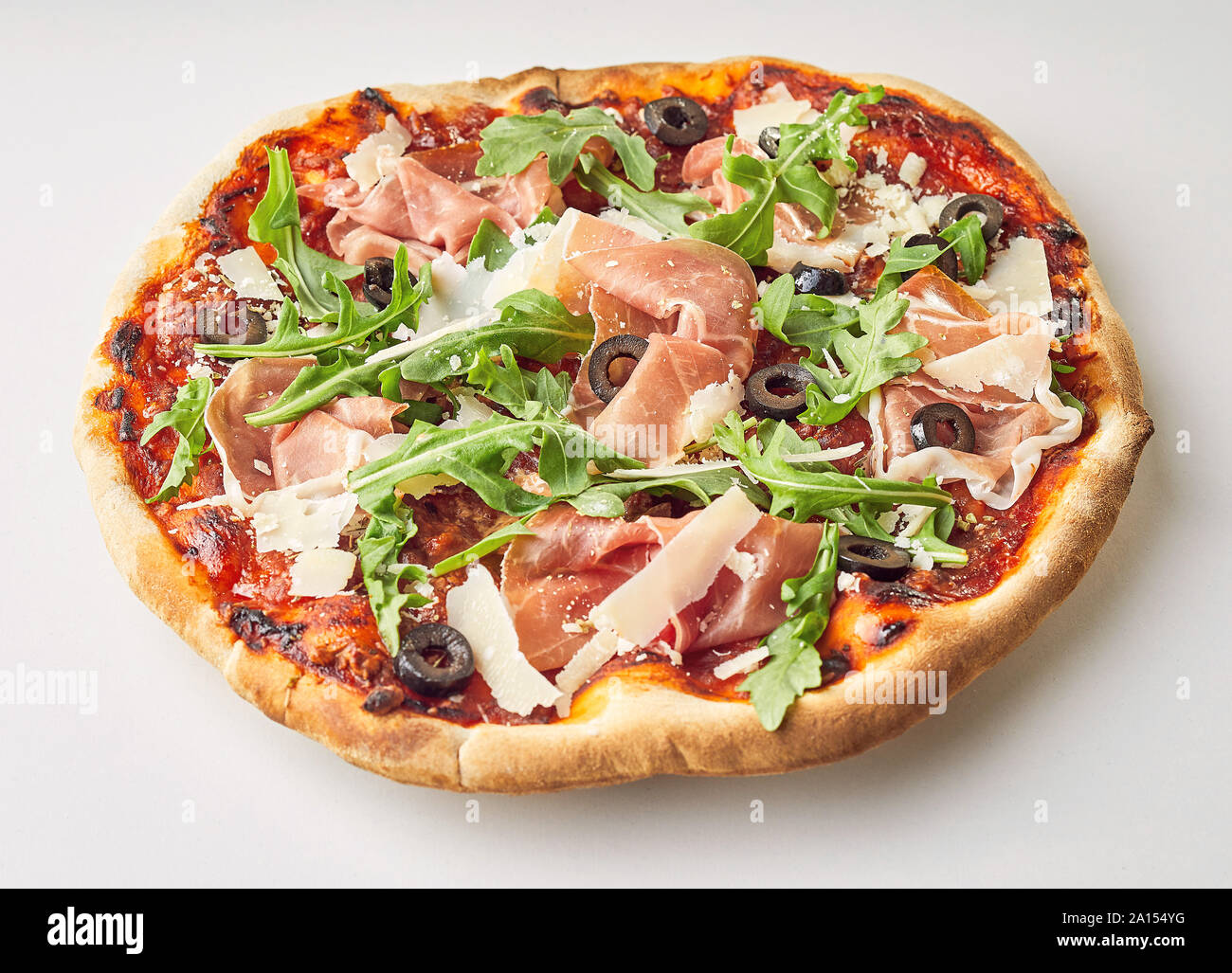Leckere Schinken, Rucola und Parmesan Olivenöl italienische Pizza mit Käse und Tomaten auf eine knusprige Ofen feuerte Base über Weiß Stockfoto