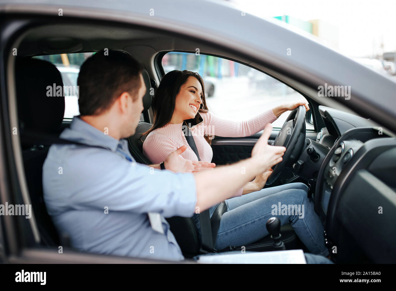 Männliche auto Kursleiter nimmt Untersuchung in der jungen Frau. Emotionale Mann point mit Hand an der Straße. Unvorsichtige junge Schülerin am Telefon sprechen und Auto Stockfoto
