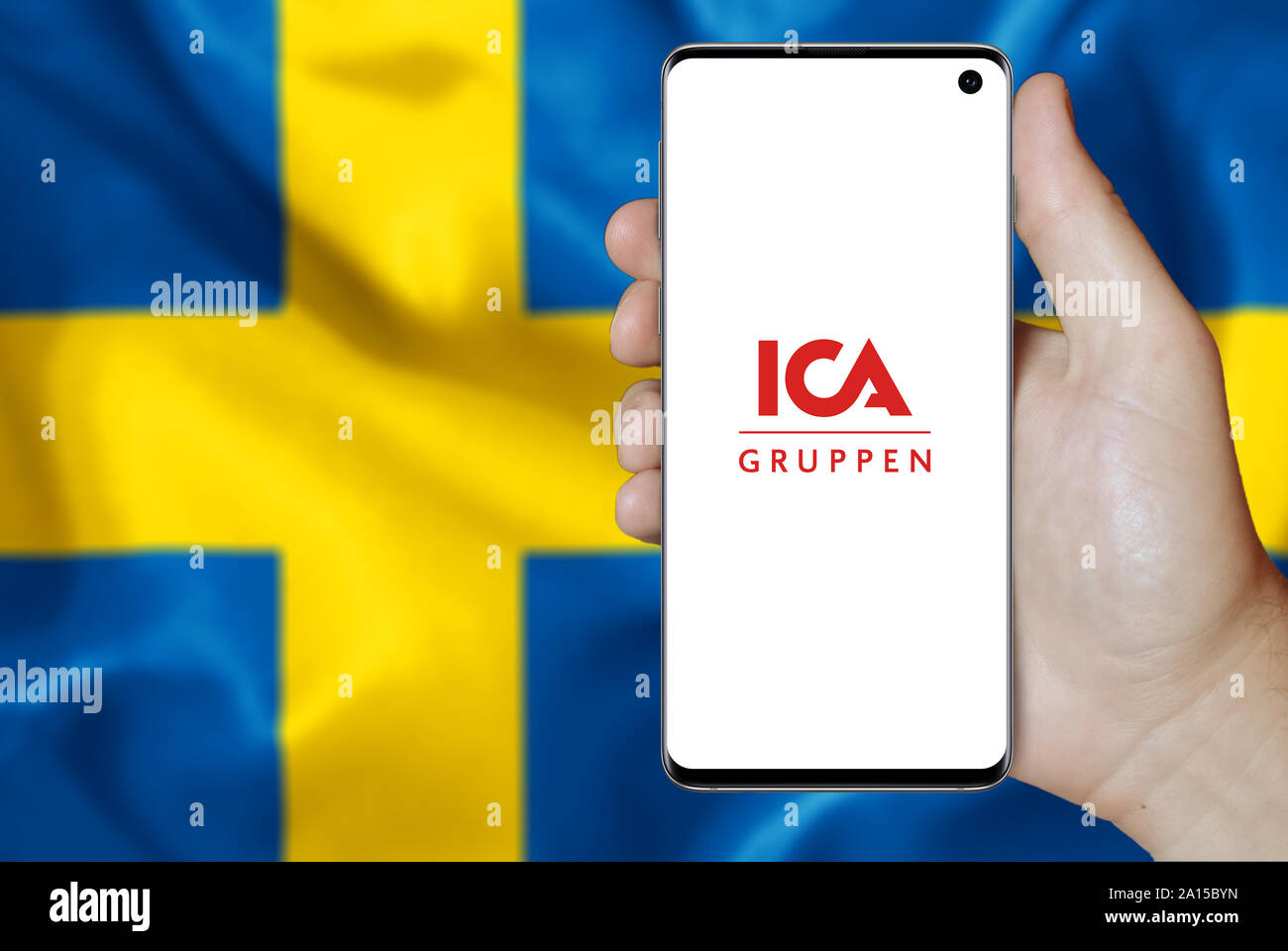 Ein Mann hält ein Smartphone mit dem Logo der Firma ICA-Gruppen im OMX Stockholm aufgeführt. Schwedische Flagge im Hintergrund. Credit: PIXDUCE Stockfoto