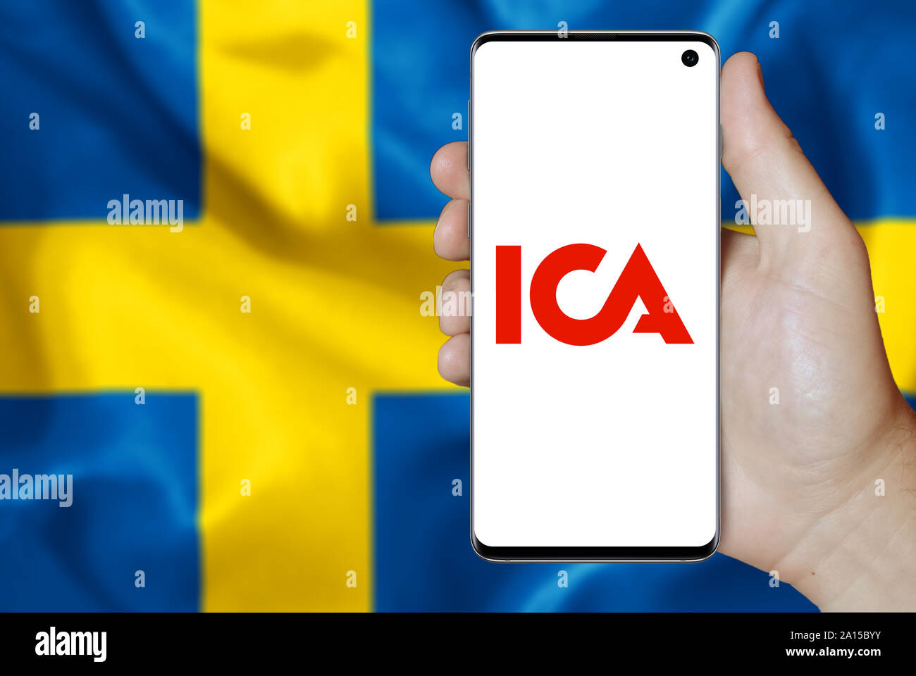 Ein Mann hält ein Smartphone mit dem Logo der Firma ICA-Gruppen im OMX Stockholm aufgeführt. Schwedische Flagge im Hintergrund. Credit: PIXDUCE Stockfoto