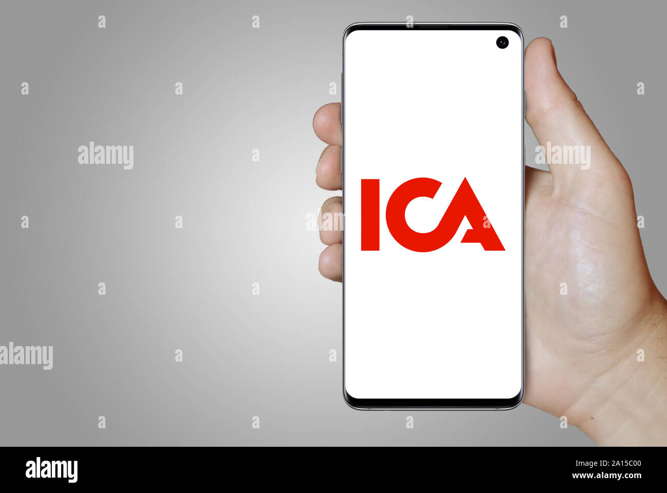 Ein Mann hält ein Smartphone mit dem Logo der Firma ICA-Gruppen im OMX Stockholm aufgeführt. Grauen Farbverlauf im Hintergrund. Credit: PIXDUCE Stockfoto