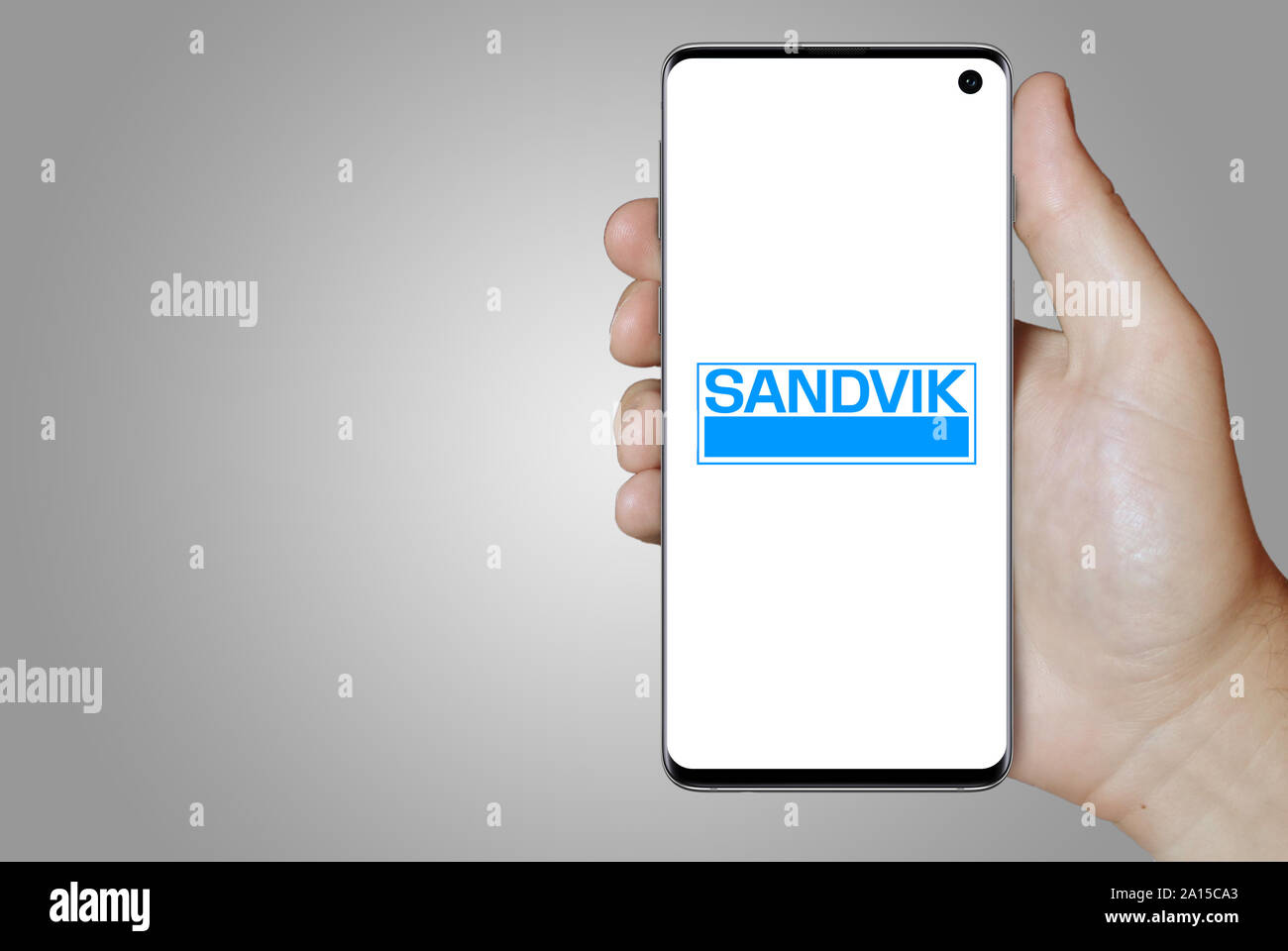 Ein Mann hält ein Smartphone mit dem Logo der Firma Sandvik im OMX Stockholm aufgeführt. Grauen Farbverlauf im Hintergrund. Credit: PIXDUCE Stockfoto