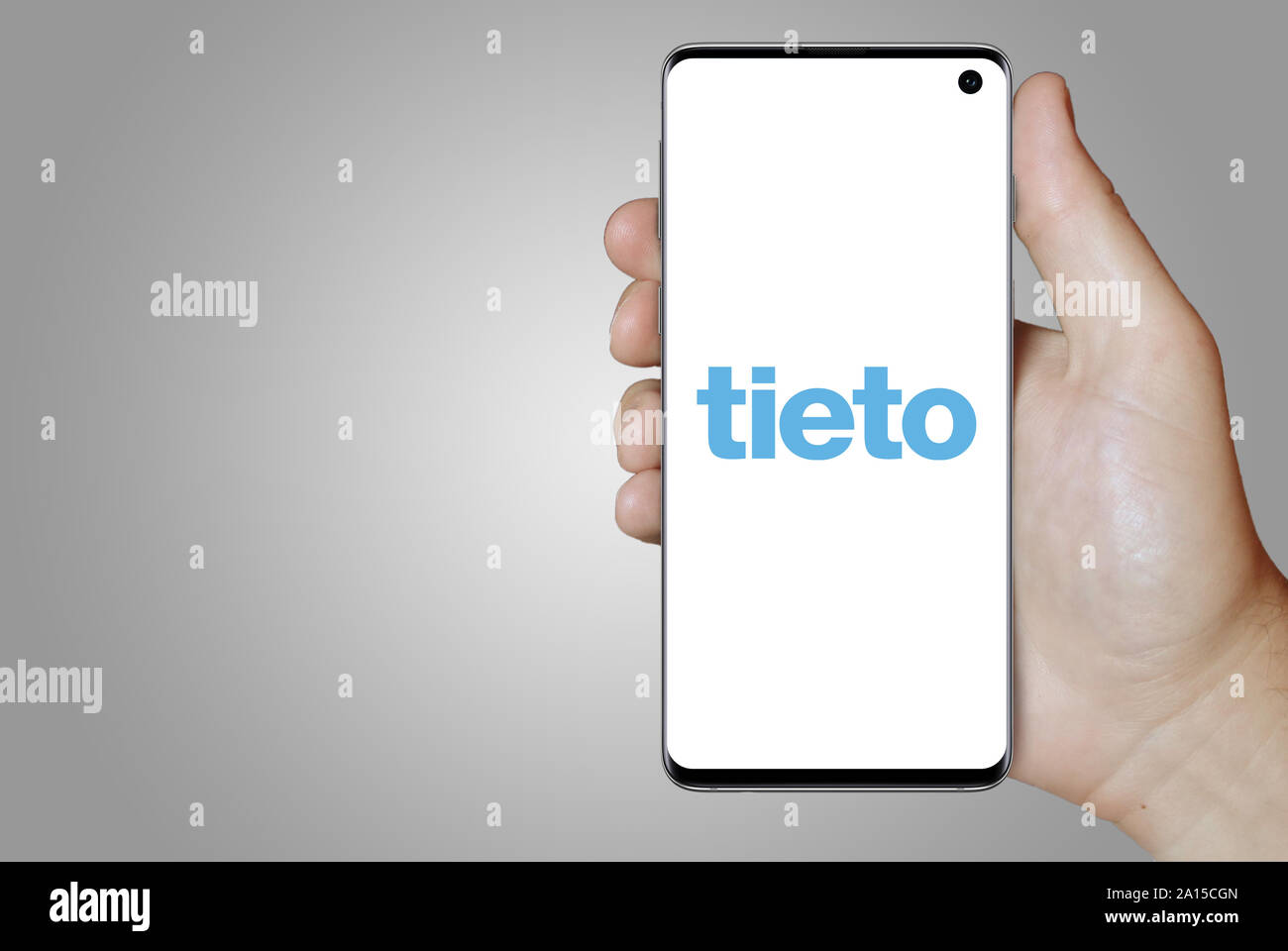 Ein Mann hält ein Smartphone mit dem Logo der Firma Tieto im OMX Stockholm aufgeführt. Grauen Farbverlauf im Hintergrund. Credit: PIXDUCE Stockfoto