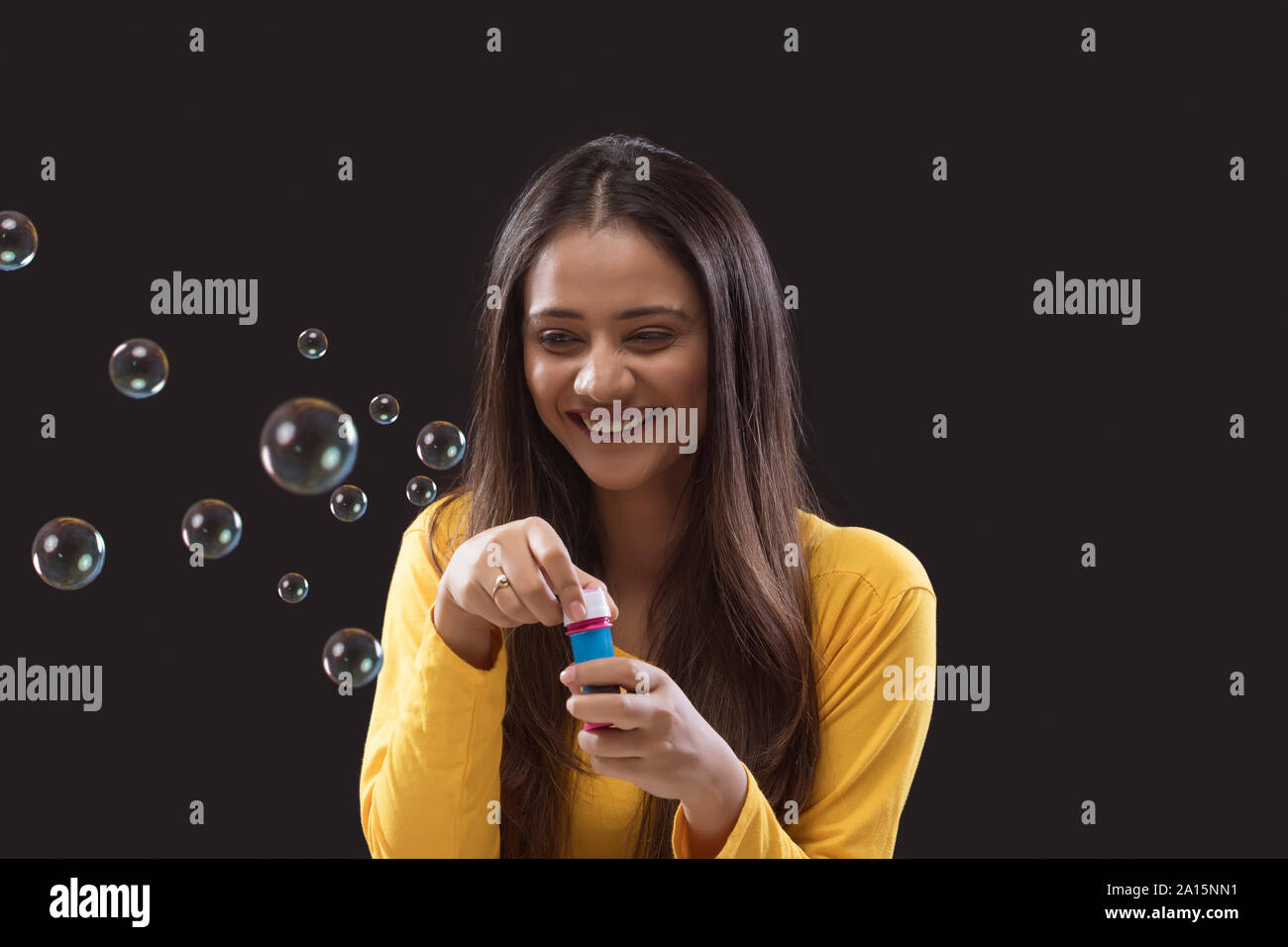 Junge Frau bläst Seifenblasen auf schwarzem Hintergrund Stockfoto