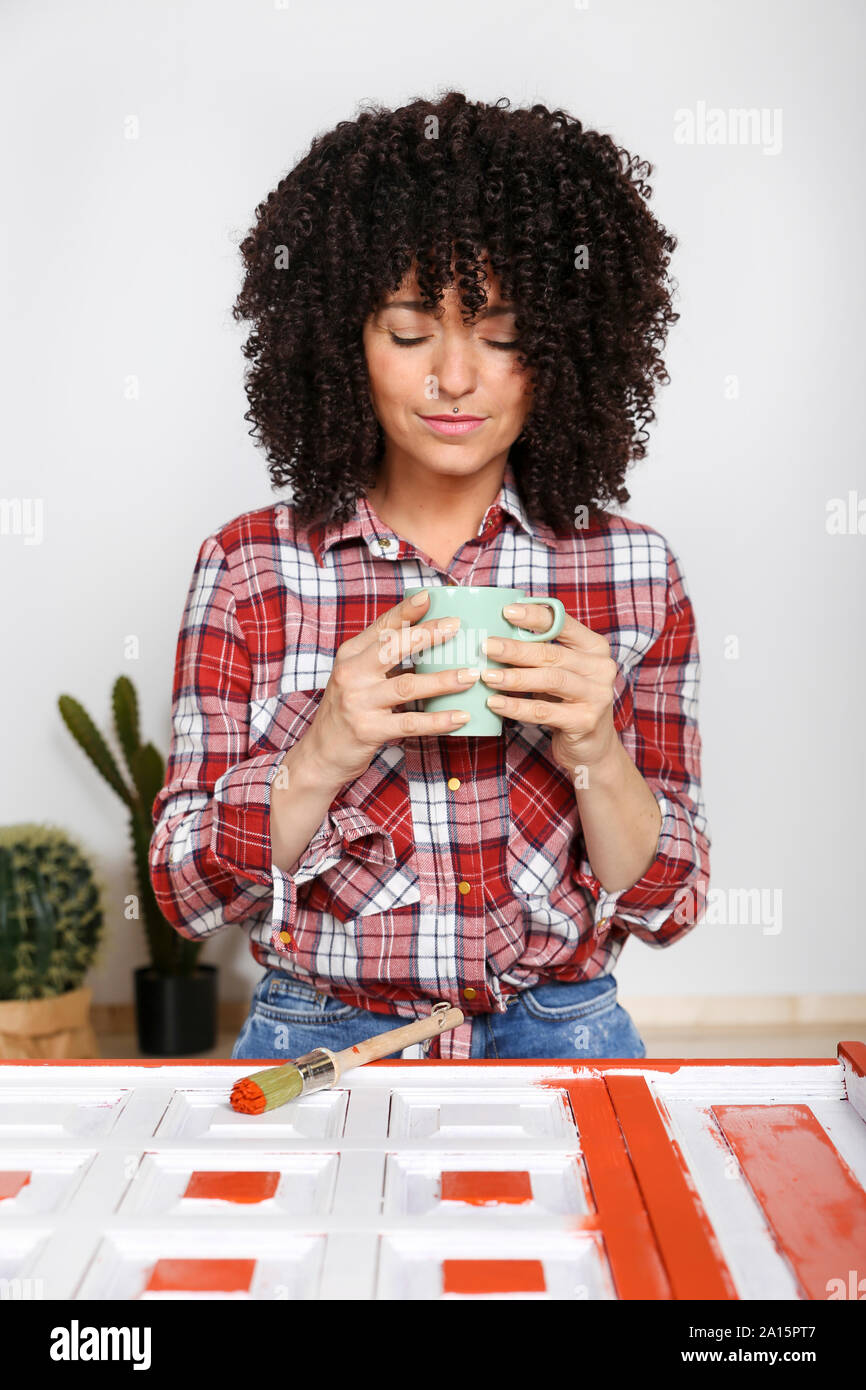 Frau mit Tasse Kaffee zu Hause, bemalte Möbel Stockfoto