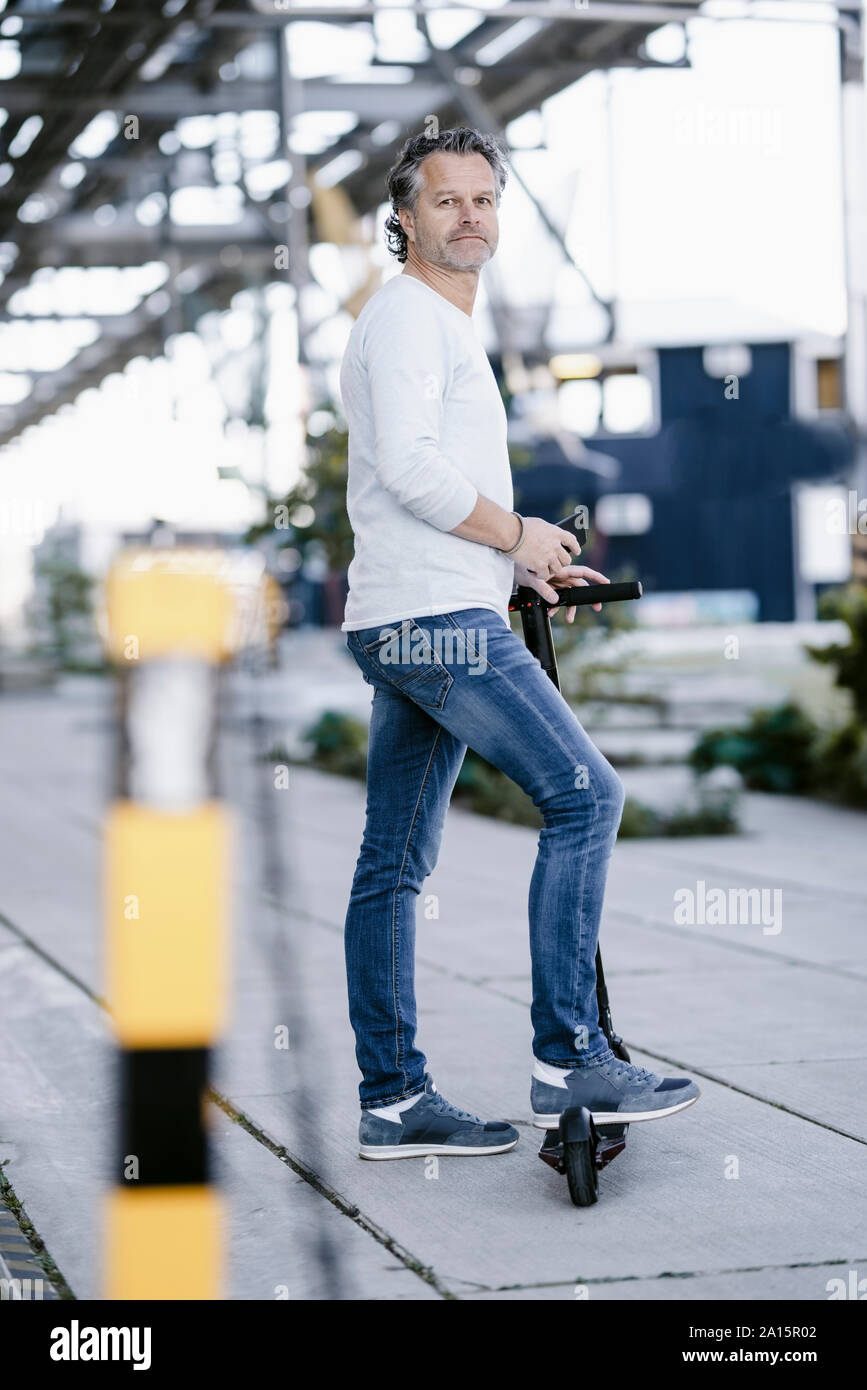 Reifer Mann mit Smartphone und Elektroroller Stockfoto