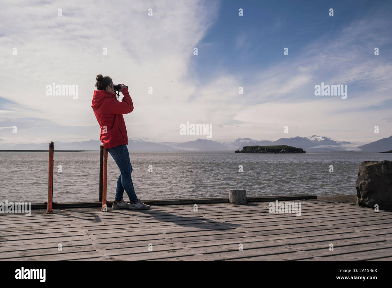 Junge Frau standig auf einem Steg und schaut durchs Fernglas, South East Iceland Stockfoto