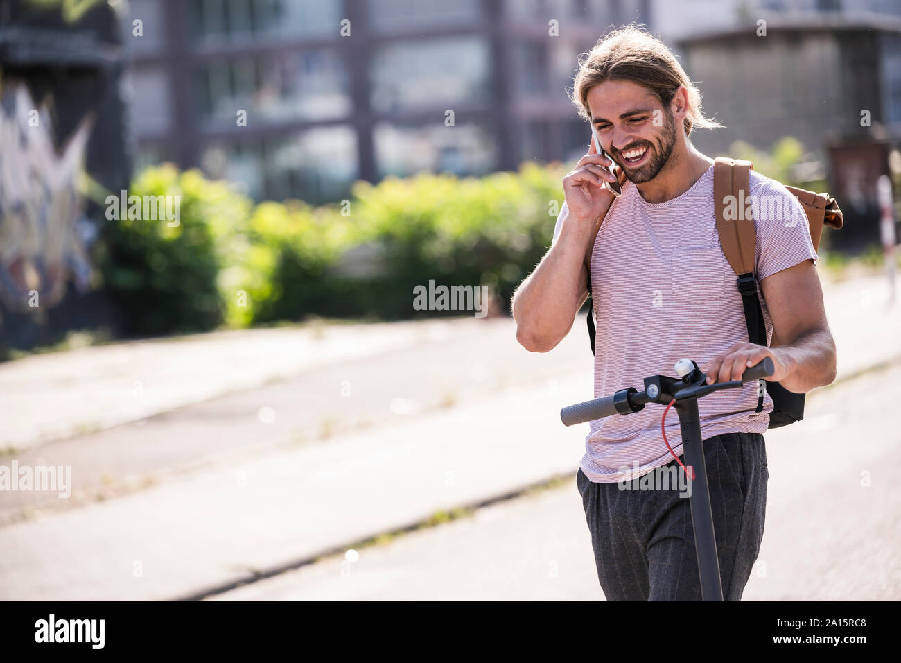 Glückliche junge Mann mit Elektroroller Telefonieren auf der Straße Stockfoto