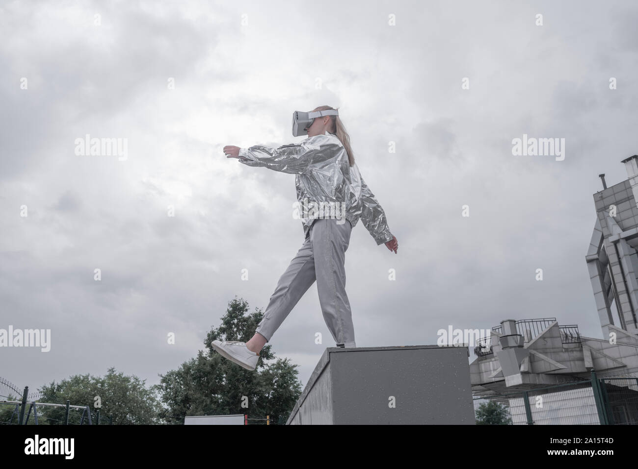 Mädchen in Silber Anzug durch VR-Brillen, stehend auf, gegen den grauen Himmel Stockfoto