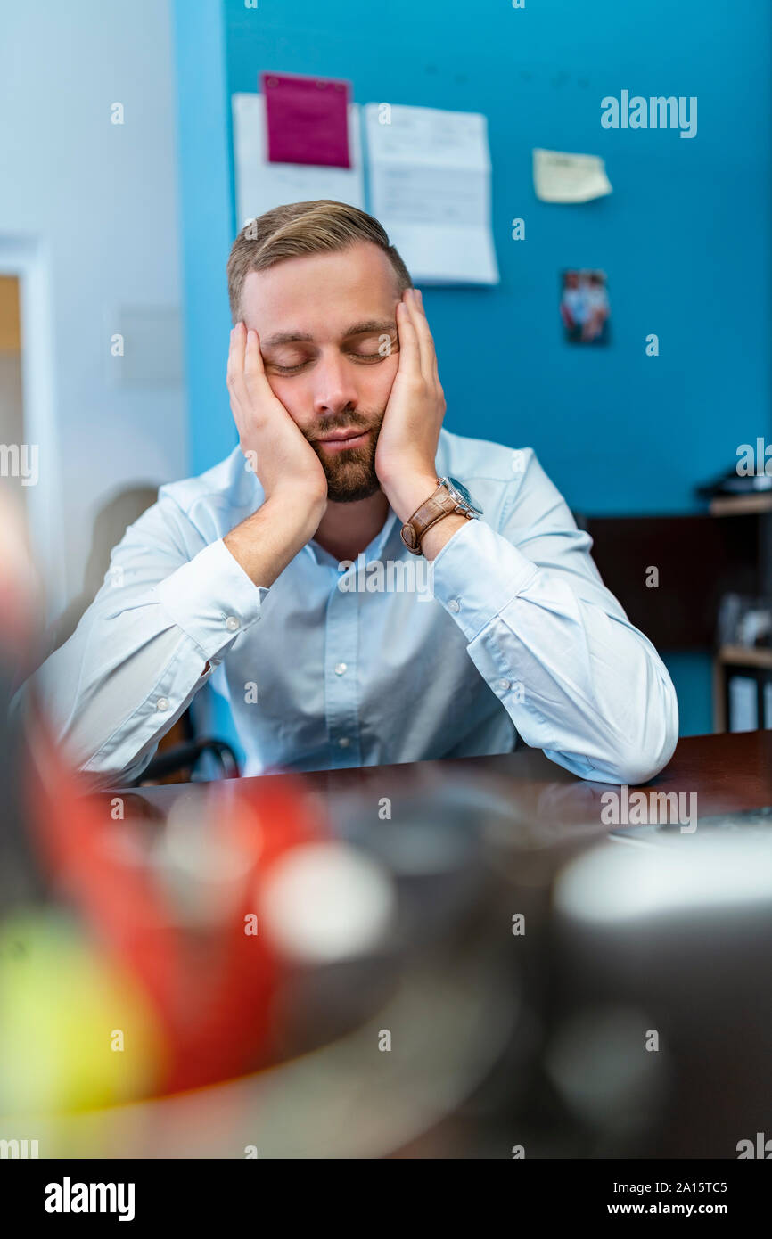 Müde Geschäftsmann mit geschlossenen Augen lehnte sich auf dem Schreibtisch im Büro Stockfoto