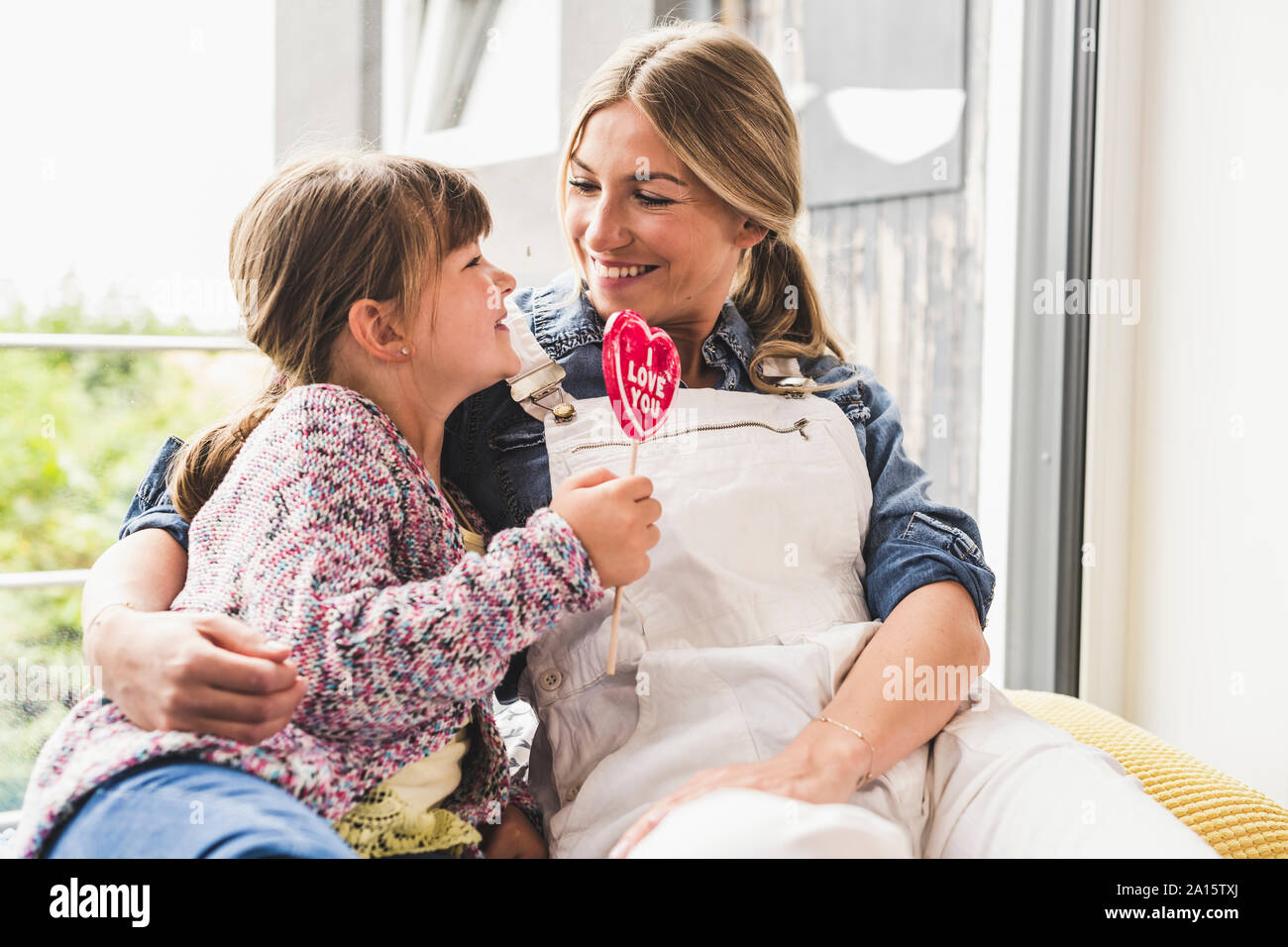 Glückliche Mutter und Tochter mit Lollipop am Fenster zu Hause Stockfoto