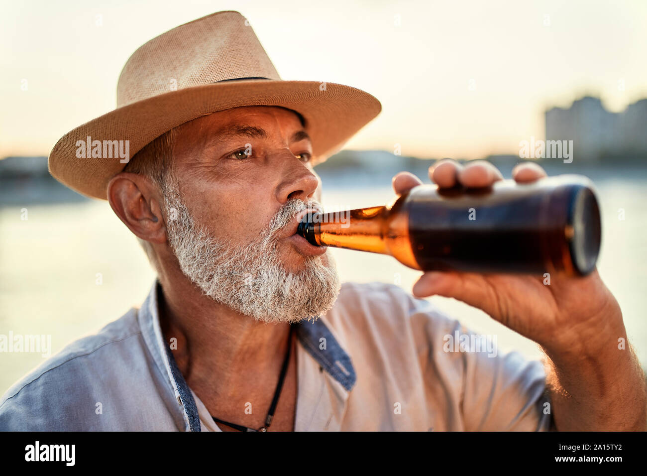 Älterer Mann ein Bier trinken im Riverside bei Sonnenuntergang Stockfoto